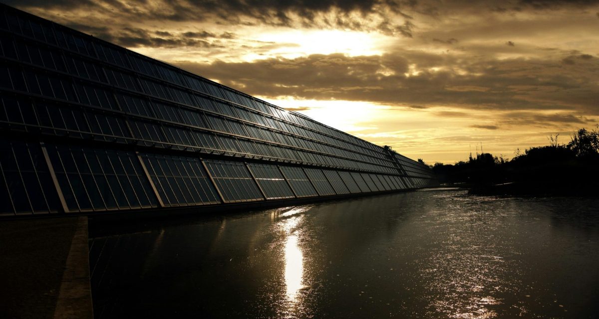 Silhouetted solar panels reflect sunset in tranquil waters, showcasing renewable energy.